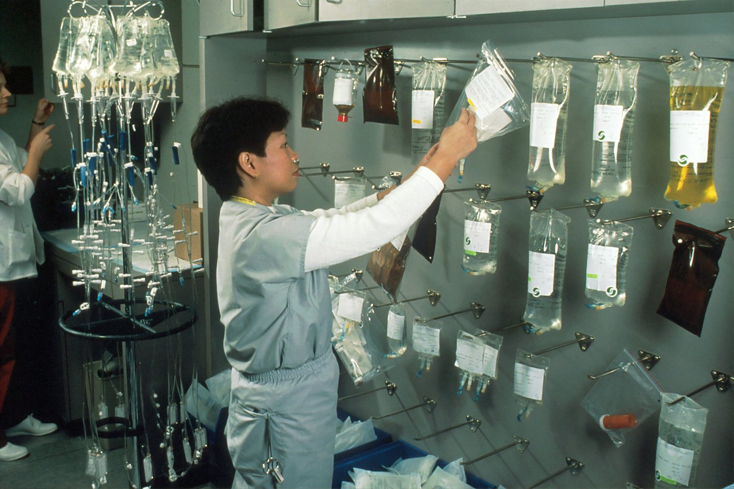 Medical professional placing fluid bag onto wall rack.