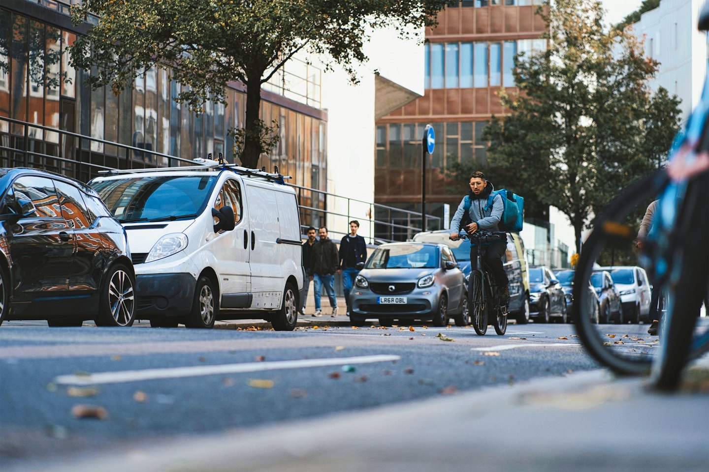 Delivery driver on bicycle with blue backpack on city street.