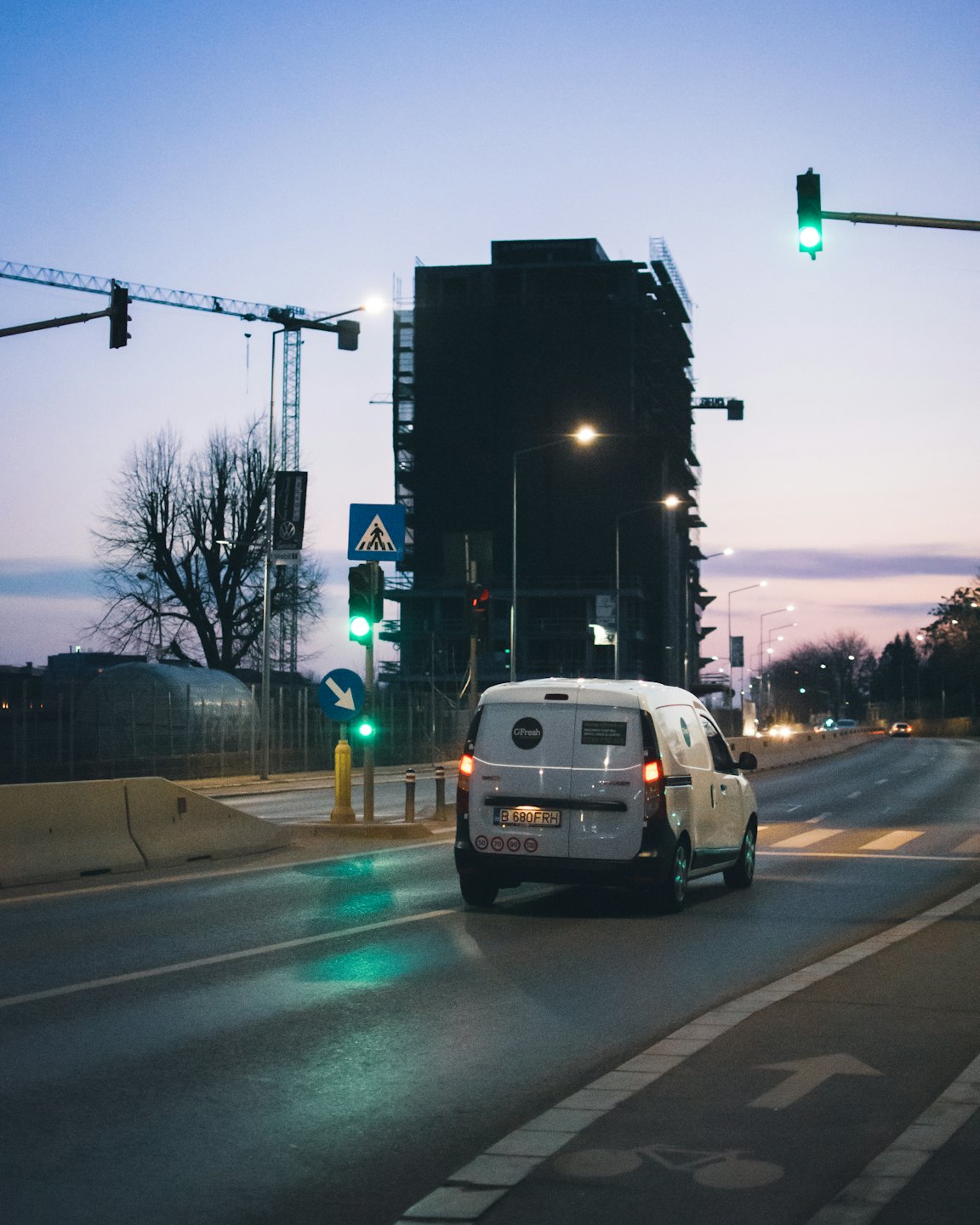 White delivery van drives away on a city street at dusk.